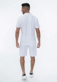 Chemise blanche à manches courtes et short, tous deux en tissu lisse, avec une coupe décontractée et des détails subtils, associés à des baskets blanches.