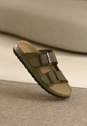 Green suede slide sandal with two adjustable black buckles, cork footbed, and textured rubber sole for grip.