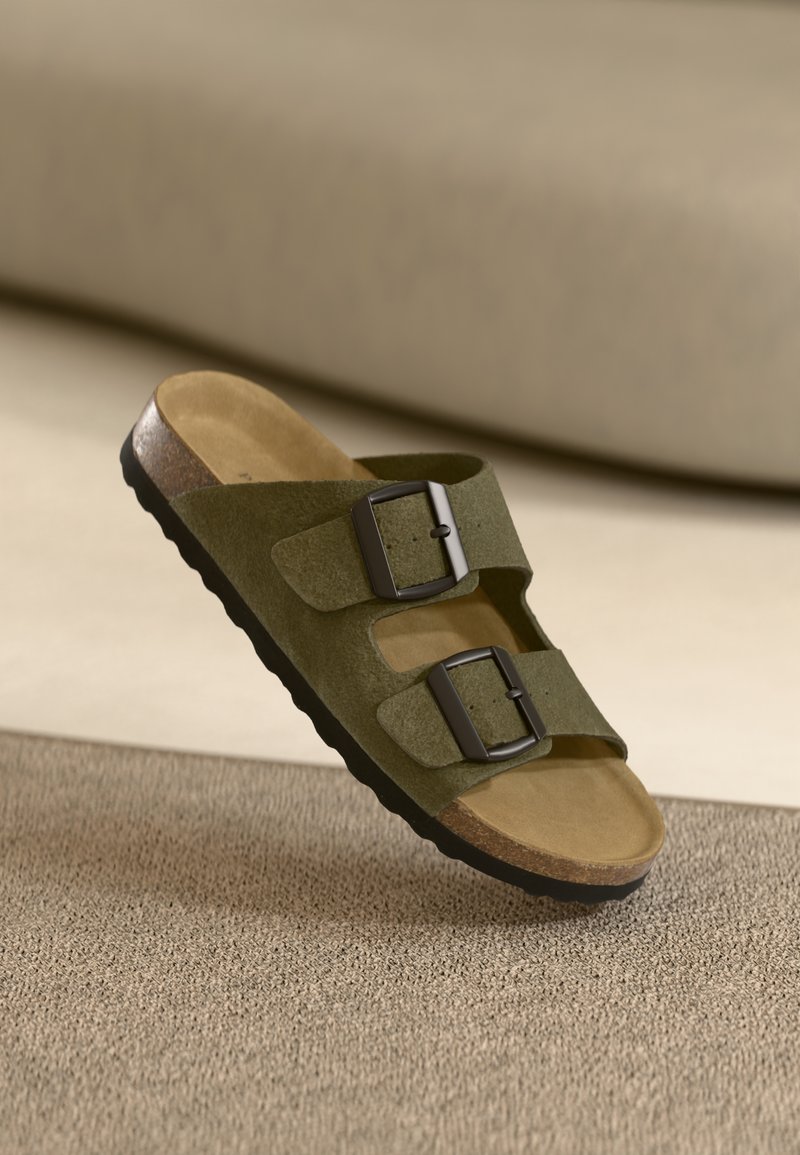 Green suede slide sandal with two adjustable black buckles, cork footbed, and textured rubber sole for grip.