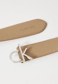 Cintura in pelle cuoio con finitura testurizzata, logo "Calvin Klein" in rilevo e fibbia in metallo argentato a forma di "CK".