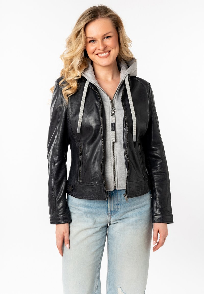 Zwarte leren jas met een aansluitend ontwerp, grijze hoodie eronder, ritssluiting aan de voorkant en geribbelde manchetten, gecombineerd met licht gewaschen jeans.