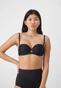 Zwarte push-up bh van gladde stof, met onderdraden ondersteuning, verstelbare bandjes en een uitsparing in het midden. Gecombineerd met hoge taille zwarte onderkleding.