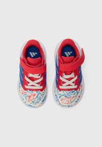 Une paire de baskets pour tout-petits avec des sangles rouges, des lacets blancs, des rayures bleues et des motifs de dinosaures en rouge et bleu sur fond blanc.