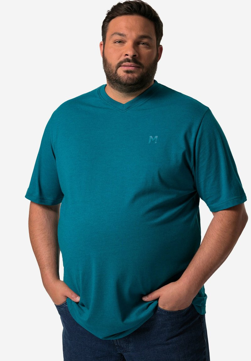 Tyrkysové tričko s výstřihem do V vyrobené z měkkého materiálu; má krátké rukávy a decentní logo na hrudi. Nosené s tmavě modrými džínami.