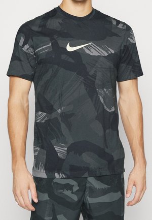 Homme portant un T-shirt Nike noir et gris à motif camouflage abstrait et un short assorti, debout avec les bras détendus le long du corps.