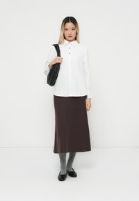 Vit skjorta med lång ärm, brun kjol, grå strumpor som går upp till låren och svarta ballerina-skor. Inkluderar en svart axelväska. Minimalistisk design.