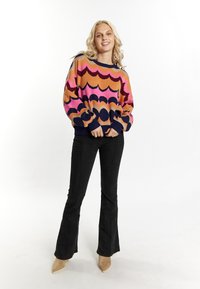 Maglione lavorato a maglia multicolore con motivi a onda in tonalità di rosa, arancione e blu navy. Abbinato a jeans neri svasati e tacchi color beige.