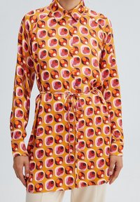 Long-sleeve shirt dress with yellow, orange, pink, and red geometric circle pattern, buttoned front, and waist tie belt.