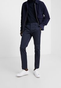 Námořnická kordová bunda přes tmavou košili, doplněná o přizpůsobené námořnické kalhoty a bílé tenisky. Hladké materiály a ležérní design.