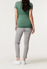 Vihreä lyhythihainen tiukka paita yhdistettynä vaaleanharmaisiin slim fit -farkkuihin. Farkuissa on pieni halkio nilkassa, ja asusteena valkoiset lenkkarit.