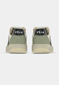 Zapatillas verdes y crema con parte superior de ante texturizado, punta redondeada y suela beige gruesa. Logo negro "VEJA" en la parte trasera.