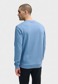 Ljusblå sweatshirt i mjukt tyg, med rund hals och långa ärmar. Designen har en slät yta och ribbade manschetter.