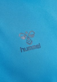 Blåt stof med mørkegrå stiliseret humlebi-logo over ordet "hummel" skrevet med små bogstaver på sportstøjsmateriale.
