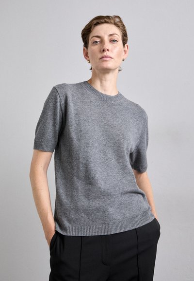 Pulover gri cu mânecă scurtă, textură tricotată, gât rotund, croială lejeră, asortat cu pantaloni negri. Material moale, ușor, cu un design minimalist.