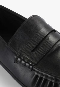 Mocasines de cuero negro con una banda cosida en la parte superior y detalles texturizados a lo largo del borde. Acabado suave con punta redonda.