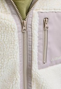 Fleecejack met een crèmekleurige textuur, voorzien van een beige ritssluiting, zijzakken en een klein logo aan de voorkant.