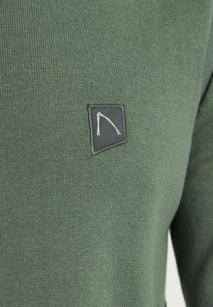 Dunkelgrüner Pullover mit strukturierter Ripp-Optik, ausgestattet mit einem schwarzen gestickten Logo-Patch in der oberen linken Ecke.