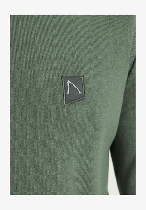 Pull vert foncé avec une texture côtelée, comportant un patch logo noir brodé dans le coin supérieur gauche.
