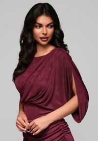 Robe de couleur vin, texturée, avec des manches drapées et un ruché sur le côté. Elle présente un tissu doux et une silhouette élégante.