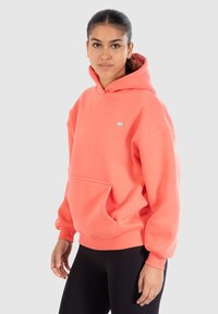 Felpa cappuccio rosa corallo realizzata in tessuto morbido, con tasca frontale, polsi a costine e un piccolo logo sul petto.