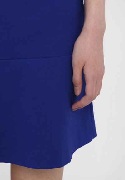 Rochie albastru regal cu un corset ajustat și fustă Evazată. Textură netedă, fără modele sau elemente metalice vizibile. O mână este odihnită pe țesătură.