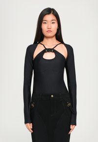 Bodysuit preto de mangas longas com detalhe recortado no peito, tecido texturizado, corte justo, com um nó na gola, combinado com jeans pretos.