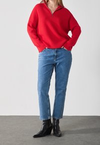 Jersey rojo de punto acanalado con cuello con cremallera, combinado con vaqueros de pierna recta en azul claro y botines de cuña negros.