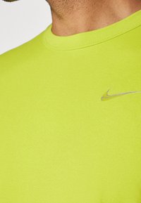 Acercamiento de una persona que lleva una camiseta Nike de color verde lima con un pequeño logo plateado de swoosh de Nike en el pecho.