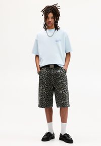 Lyseblå oversized t-shirt med et lille grafisk motiv, parret med grønne leopardprint shorts, sort bælte og sorte sko med hvide sokker.