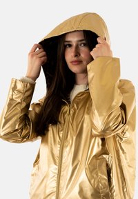 Veste à capuche dorée brillante avec une fermeture éclair sur le devant, des poches latérales et une doublure en imprimé léopard dans la capuche ; texture lisse, design léger.