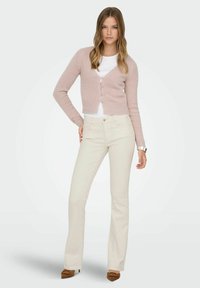 Light pink cropped cardigan with round neckline, button closure, and long sleeves, paired with cream flared jeans and brown heeled shoes.