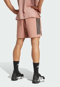 Shorts de sport roses avec un design à trois bandes noires, associés à des chaussettes montantes noires et des baskets noires avec des accents blancs.