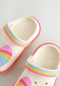 Valged klotsid kummist välisküljega, millel on värvikas vikerkaarepael, südamekujundus ning roosad detailid tallal ja rihmal.