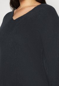 Dark gray knit sweater with a V-neck, featuring a textured fabric and long sleeves, emphasizing a relaxed fit and ribbed detailing.