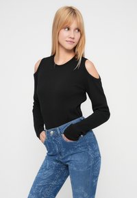 Μαύρο μπλουζάκι με μακριά μανίκια και κομμένες ώμους, σε συνδυασμό με ανοιχτό μπλε τζιν με floral σχέδιο και ψηλή μέση.