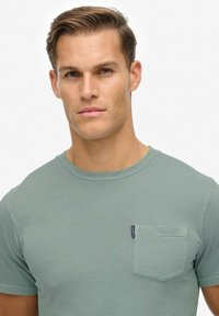 Grøn kortærmet T-shirt lavet af blød bomuld, med en frontlomme, og har et rundhalset design. Enkel og uprydet udseende.