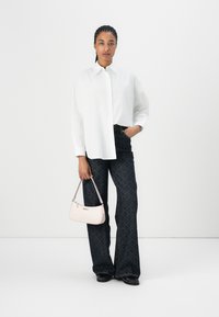 Weißes Hemd mit Knöpfen, dunkel gemusterte Schlagjeans und eine kleine blassrosa Handtasche mit einem Riemen. Schwarze Schuhe runden das Outfit ab.