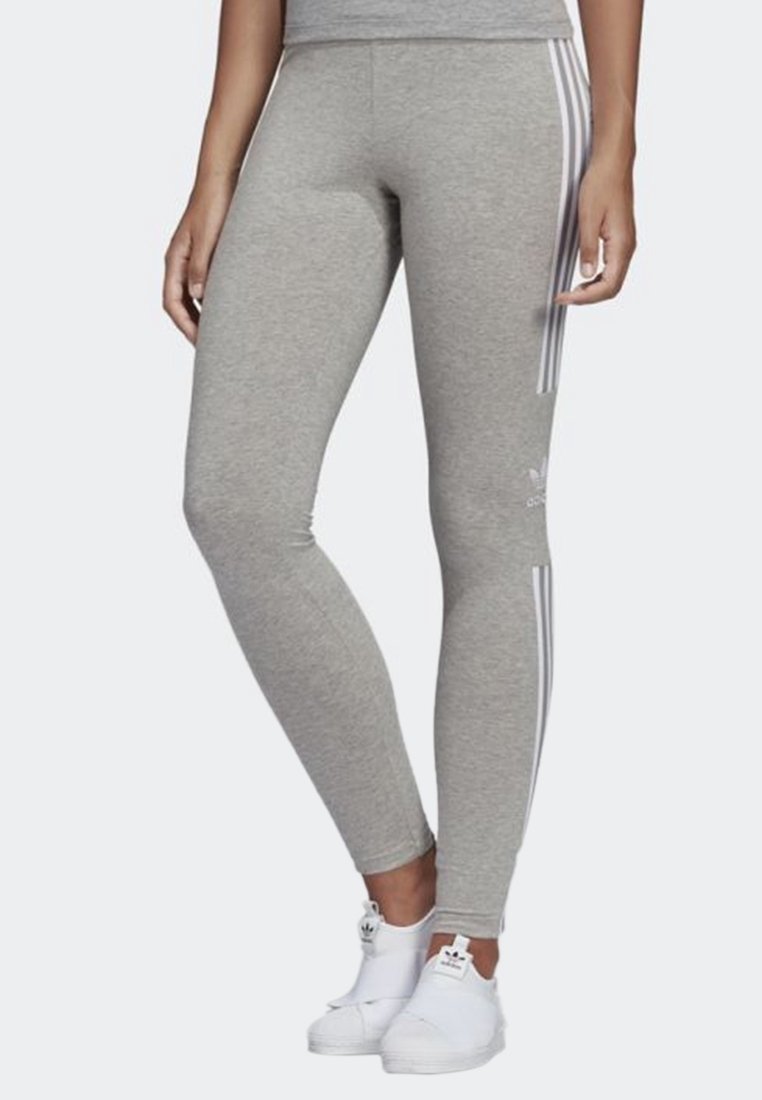 Leggings grigi realizzati in tessuto morbido, con tre strisce bianche verticali lungo i lati e un logo Adidas alla caviglia.