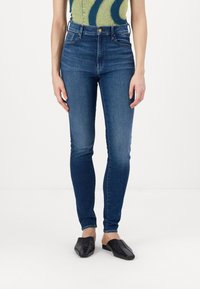 Skinny jeans in dark blue denim, high-waisted with a smooth texture. Finished with a gold button and minimalistic front pockets.