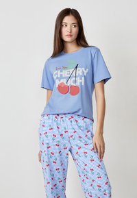 T-shirt in cotone azzurro con stampa grafica di ciliegie, abbinato a pantaloni da pigiama a scacchi con motivi di ciliegie su sfondo blu.