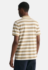 Polo de manga corta con rayas horizontales en beige y blanco, hecho de algodón suave, con un collar clásico y aberturas laterales.
