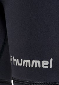 Sorte atletiske shorts lavet af strækbart stof, med en glat overflade og hvid "hummel" logo trykt på siden.