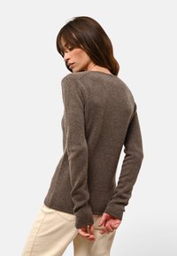 Brauner Pullover mit langen Ärmeln aus weichem Strickstoff, mit gerippten Bündchen und Rundhalsausschnitt. Er hat ein körperbetontes Design und eine subtile Textur.