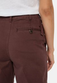 Maroon pants with a smooth texture, featuring a back pocket, button closure, and minimal stitching details.