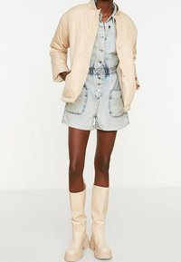 Blød beige quiltet jakke, chambray button-up romper i lysvasket denim og knæhøje beige læderstøvler med tykke såler.