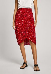 Rote blumige Midirock mit Wickeldesign, ausgestattet mit einem hohen Schlitz und einem strukturierten Stoff. Kombiniert mit schwarzen flachen Sandalen.