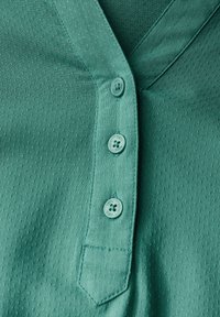 Camisetta corta manica color verde acqua con superficie testurizzata, scollatura a V e tre bottoncini di chiusura. Presenta una piccola tasca a toppa sul lato sinistro.