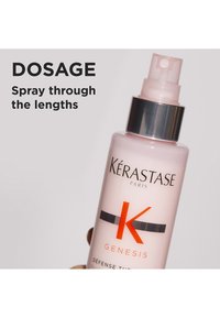 Kérastase Genesis sprayflaske i rosa plast med sølvfarget hette, med oransje 'K'-logo og doseringsinstruksjoner i fet svart skrift.