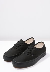 Baskets en toile noire avec semelles en caoutchouc, bout rond et design à lacets. Présentent le logo Vans sur le côté et une surface texturée.