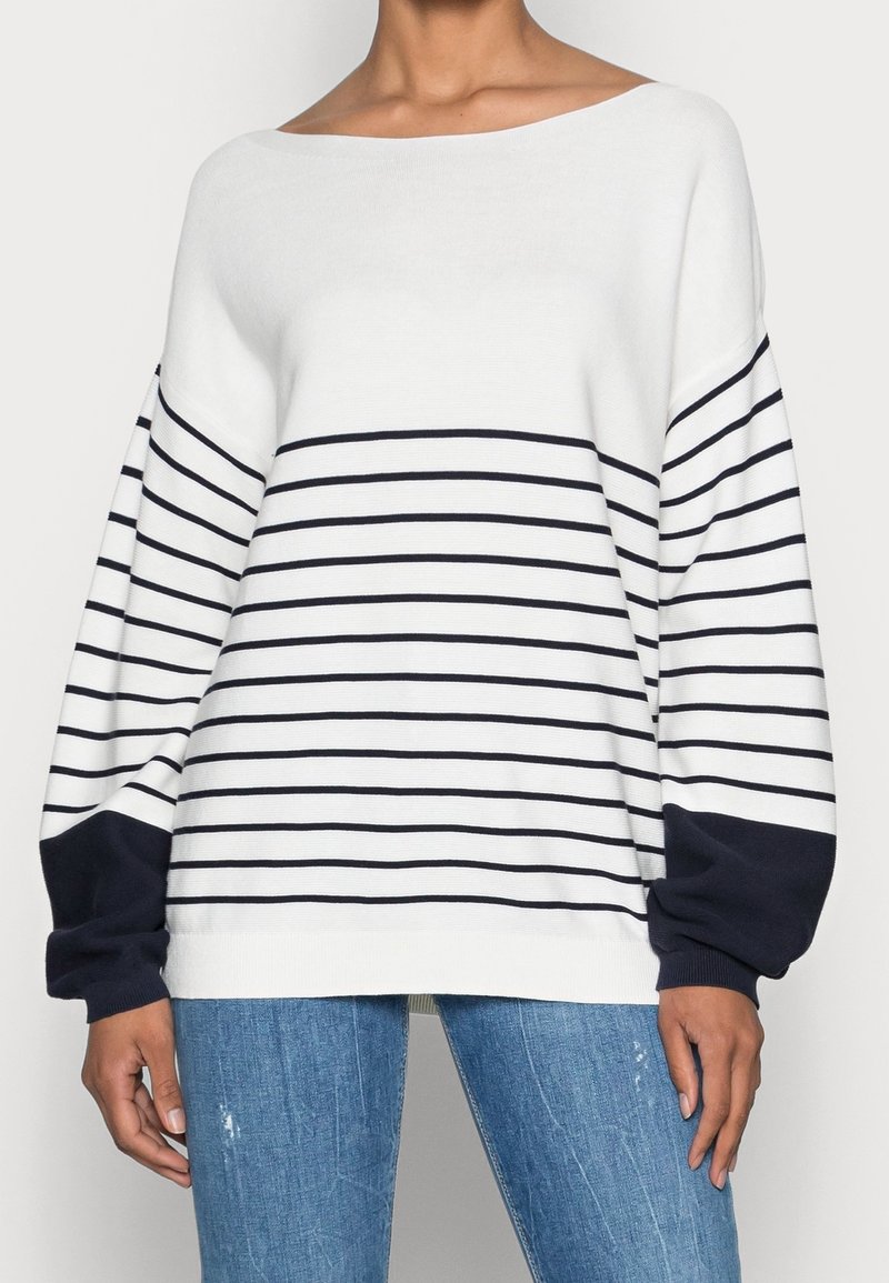 Vit och marinrandig långärmad tröja med båtutskurna hals, puffärmar och marinblå manschetter, kombinerad med blå jeans.